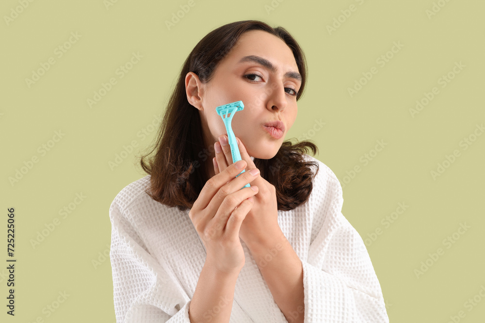 Beautiful young woman in bathrobe with razor on green background