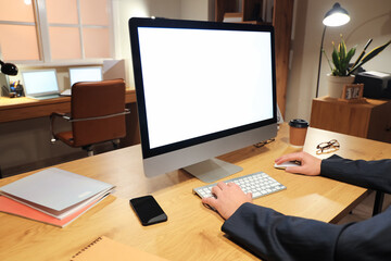 Man working with blank computer on table in office at night, closeup