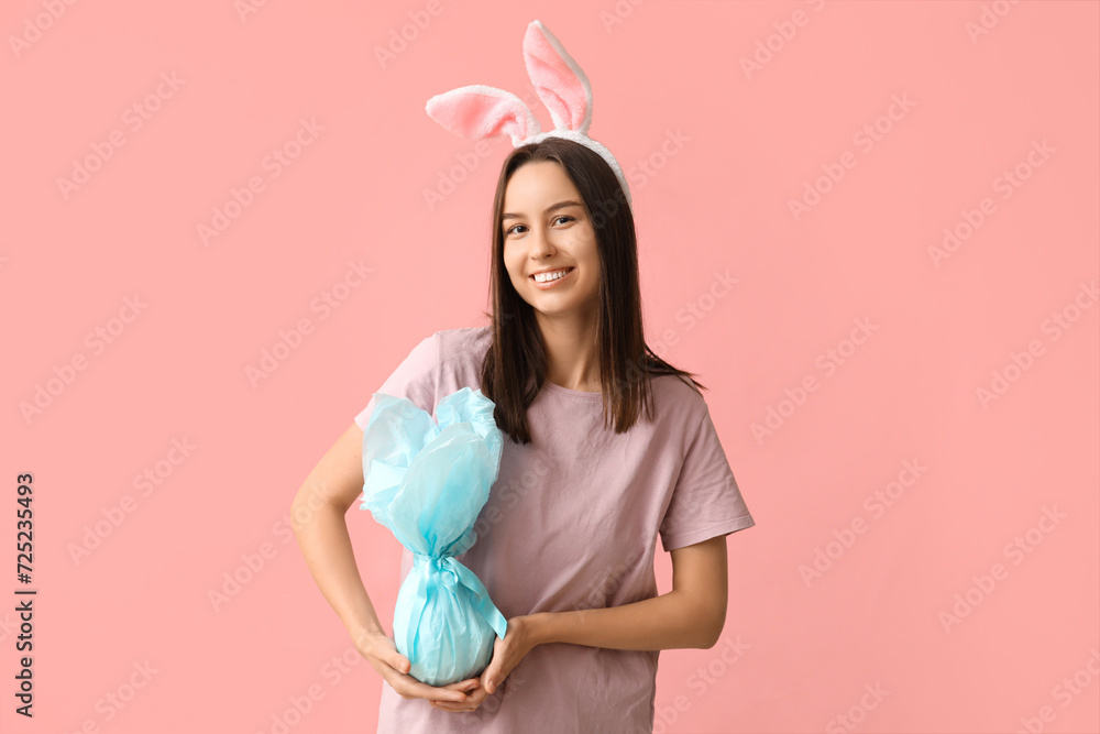 Pretty young woman with bunny ears and Easter gift on pink background