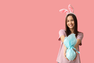 Canvas Print - Pretty young woman with bunny ears and Easter gift on pink background