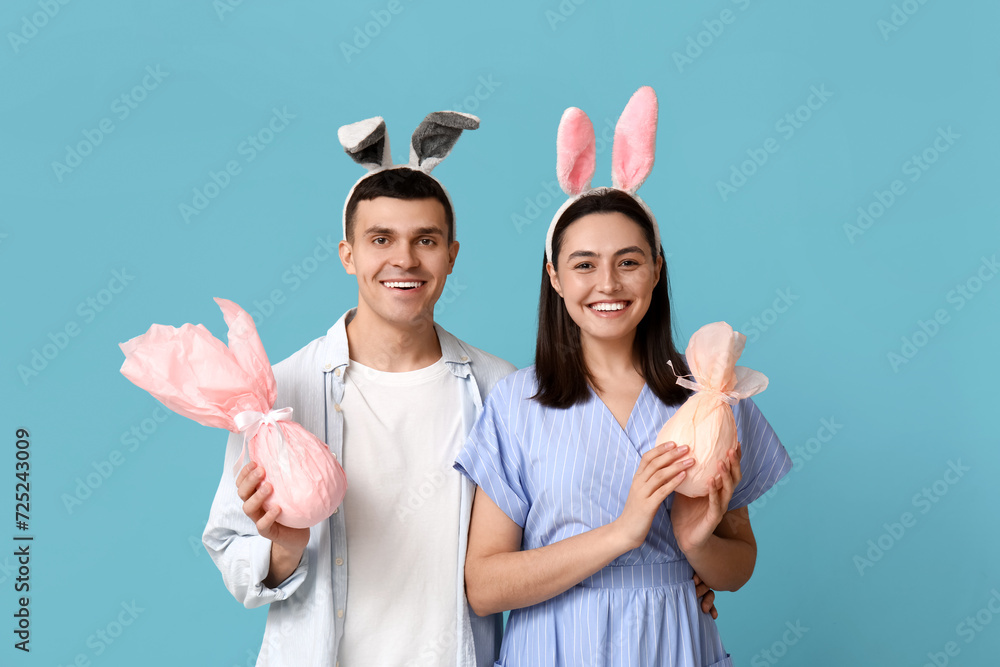 Happy young couple with Easter bunny ears and gifts on blue background