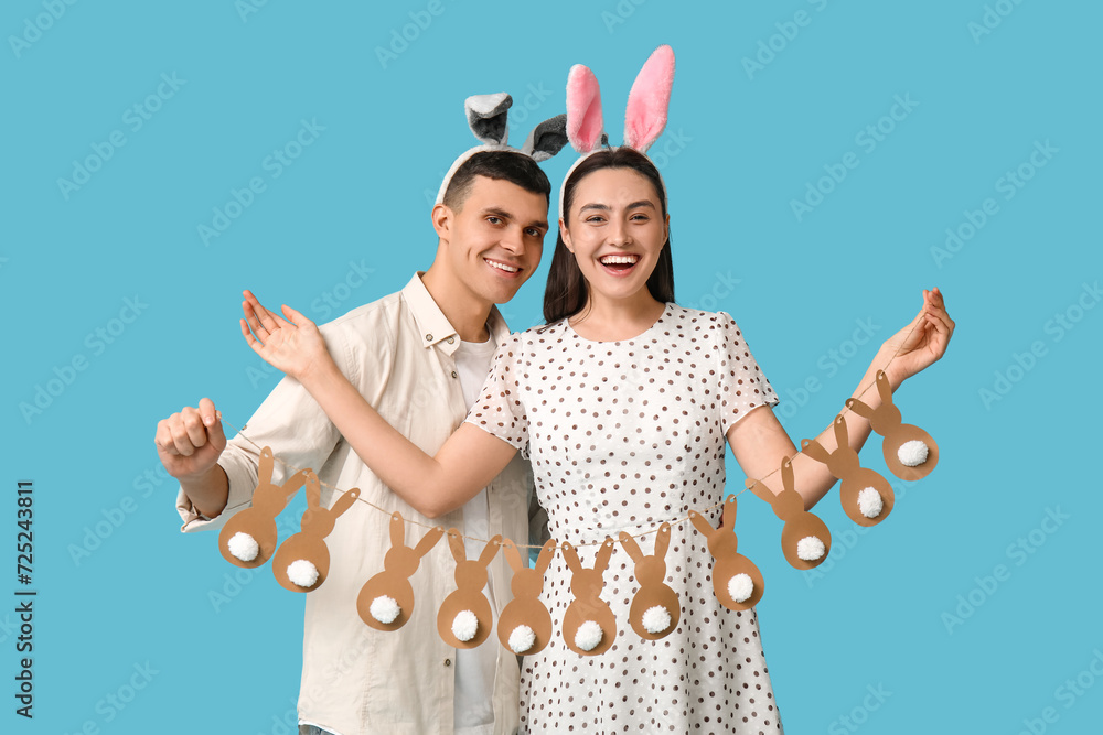 Happy young couple with Easter garland and bunny ears on blue background