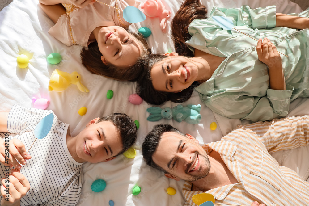 Happy family with Easter rabbits and eggs lying on bed, top view