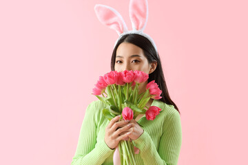 Poster - Young Asian woman in bunny ears with tulips on pink background. Easter celebration