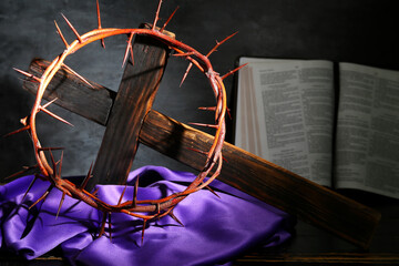 Wall Mural - Wooden cross with crown of thorns, Bible and purple cloth on grey grunge background