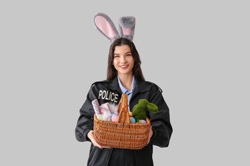 Wall Mural - Female police officer in bunny ears with Easter eggs on light background