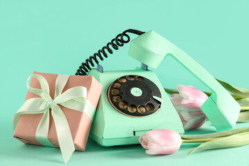 Retro telephone with beautiful tulips and gift box on turquoise background. International Women's Day