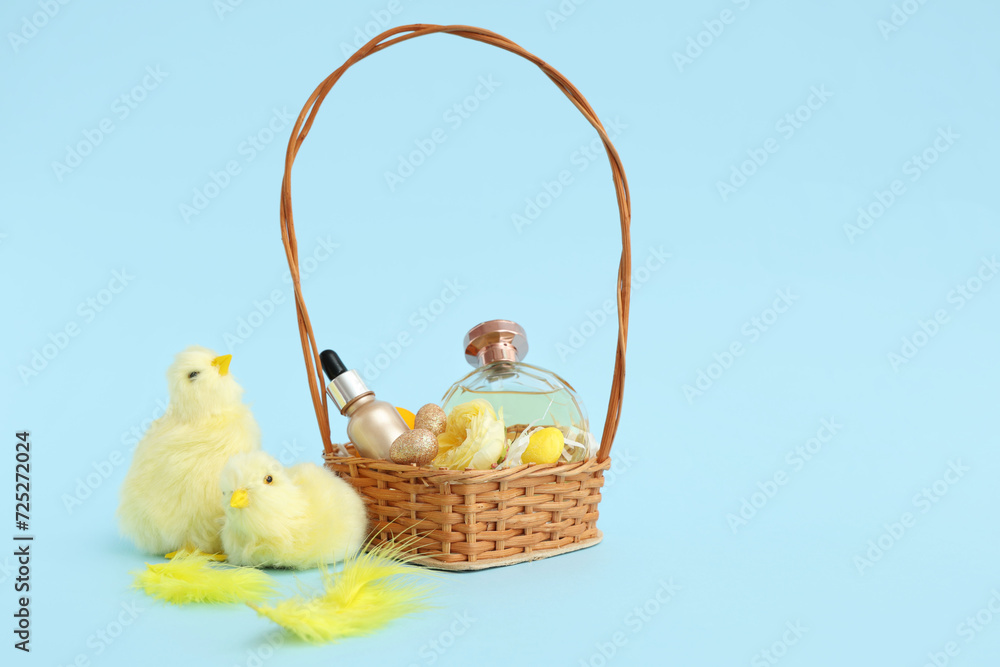 Wicker basket with decorative cosmetics, Easter eggs and baby chickens on blue background