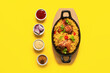Baking dish of traditional chicken biryani with ingredients on yellow background