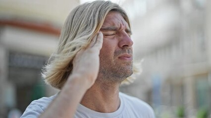 Wall Mural - A pained man with long blond hair experiencing a headache outdoors in the city.