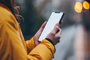 Young woman in yellow jacket using mobile phone with blank white screen.