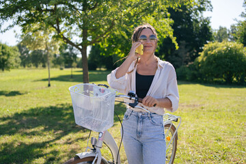 Wall Mural - European young woman in park with bicycle and talking on mobile phone. 