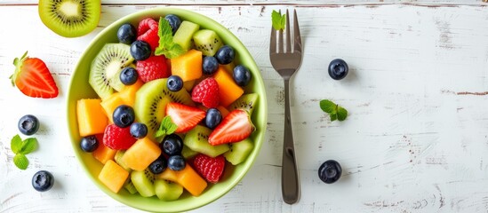 Wall Mural - White table top view with a green bowl of fruit salad, blueberries, and a fork, copy space available.