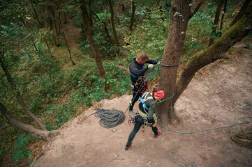 Wall Mural - Top view. Man and woman doing climbing in forest with use of safety equipment