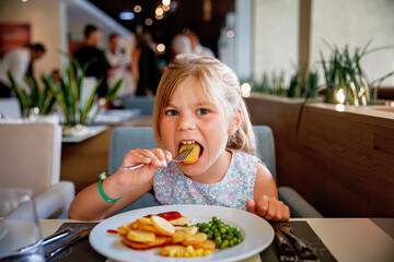 Wall Mural - Adorable little girl having breakfast at resort restaurant. Happy preschool child eating healthy food, vegetables and eggs in the morning.