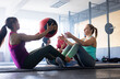 © Wavebreak Media - Side view of diverse young females passing fitness ball while sitting on floor in health club