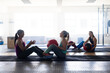 © Wavebreak Media - Side view of multiracial young females passing fitness balls while sitting on floor in health club