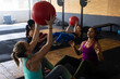 © Wavebreak Media - Diverse females throwing fitness ball to each other while sitting on floor in health club