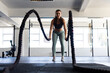© Wavebreak Media - Dedicated caucasian young woman training with battle ropes in health club against window, copy space