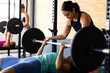 © Wavebreak Media - Diverse young woman assisting friend in lifting barbell while lying on exercise table in gym