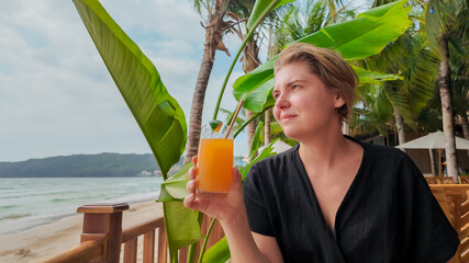 Wall Mural - A woman enjoys a tropical drink while relaxing on a beachfront, embodying vacation leisure and summer escapism