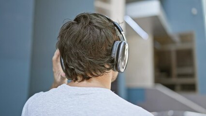 Poster - Cool young man, casually standing backwards on a sunny urban street, listening to his favorite music, lost in the sound from his headphones, a portrait of a city guy's sunny-side lifestyle