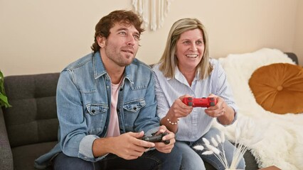 Wall Mural - Mother and son sitting on sofa together playing video game at home