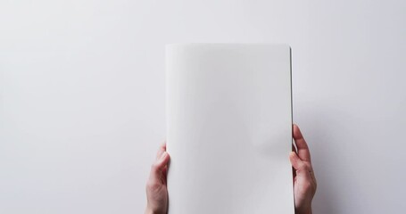 Wall Mural - Close up of hands holding book with copy space on white background in slow motion