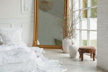 Romantic White Ruffled Bedclothes On A Bed Next To A Mirror, Stool And Two Vases