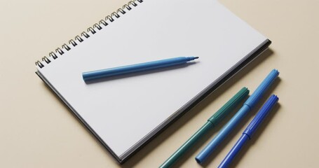 Wall Mural - Close up of notebook with blue markers on beige background, in slow motion