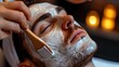 © AdriFerrer - Close-up of a facial mask being applied to a man's face with candles in the background.