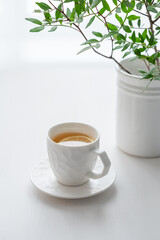 Wall Mural - A cup of tea with lemon and green branch on a white table against the background of a kitchen window.