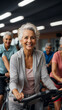 © anandart - smiling mature woman smiling  doing sports in the gym, senior people in group exercising, stationary fitness bikes in the gym