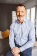 © contrastwerkstatt - Relaxed Bestager Man in Blue Shirt Sitting on Sofa, Looking Comfortable into Camera