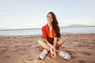 Poster - Cheerful Woman Sitting on Sandy Beach, Enjoying Vacation and Smiling Wide in Trendy Fashion Outfit