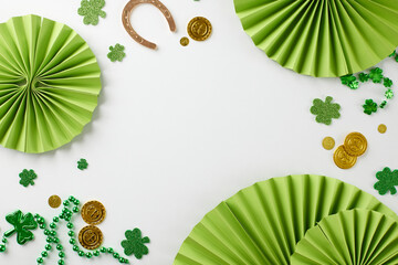 Irish bliss: St. Patrick's Day extravaganza. Top view of paper party props, trefoils, coins, horseshoe, beads on white background with well-wishing space