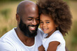 African American father with a beard hugs his curly-haired daughter and smiles.