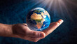 © Patrick - A small terrestrial globe on the palm of a hand with a faint radial light. World Nature Day. Concept of priceless value of wild nature.