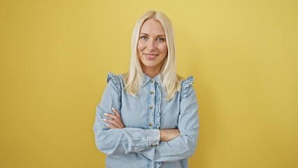 Wall Mural - Glowing portrait of a happy young blonde woman wearing a denim shirt and smiling with confidence. arms crossed, her friendly expression isolated against a cool yellow background.