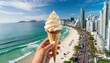 Mão segurando um cone de sorvete e ao fundo uma paisagem tropical urbana