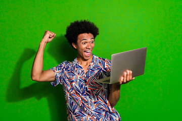 Poster - Photo of lucky impressed guy wear print shirt rising fist getting likes modern device isolated green color background