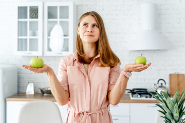 Wall Mural - Young woman choosing between green apples in the kitchen