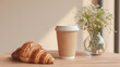 A rustic breakfast spread with a freshly baked croissant and steaming cup of coffee, set on a wooden table adorned with a delicate flowerpot and stylish serveware against a wall of warmth and comfort