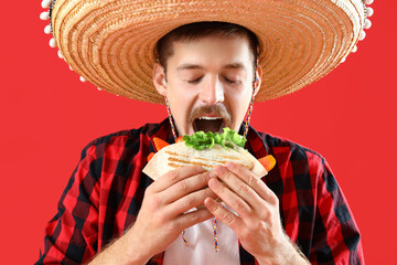 Sticker - Young Mexican man in sombrero eating taco on red background