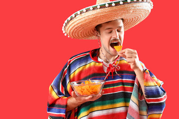 Poster - Young Mexican man eating nachos on red background