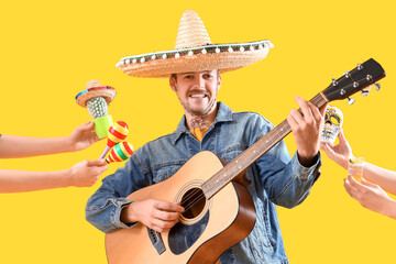 Wall Mural - Young man playing guitar and hands with Mexican symbols on yellow background