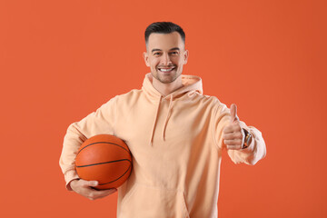 Sticker - Happy young man with ball showing thumb-up on orange background