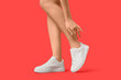 Legs of young woman in stylish white sneakers on red background