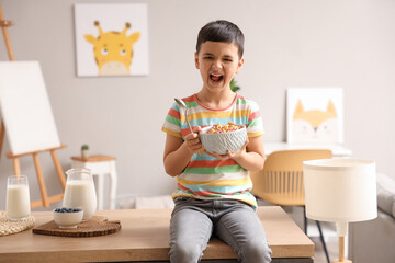 Sticker - Cute little boy with bowl of cereal rings sitting on table at home