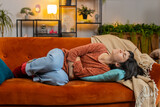 Fototapeta  - Upset young woman embracing belly suffering from stomachache lying on sofa. Unhappy Caucasian girl having menstrual painful feelings, resting on couch. Gastritis, abdominal or period pain concept